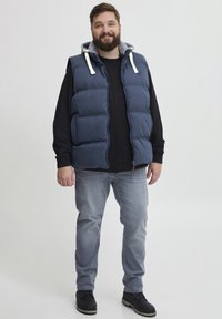 Mornarsko pufasta telovnik z sivim kapuco, sprednjim zadrgo in dvema stranskima žepoma, nosi se čez črno majico in svetlo sivo jeans hlače. Črne čevlje.