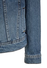 Světle modrá džínová bunda s klasickým střihem, kontrastním šitím a dvěma bočními kapsami. Tkanina má viditelnou strukturu a opotřebovaný vzhled.