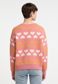 Pulover tricotat roz cu un model de inimă în crem și galben. Mâneci lungi și detalii cu tiv strâns. Textură moale.