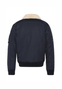 Chaqueta bombardera de color navy con un collar de piel sintética, puños y dobladillo acanalados, y una textura suave. Incluye un parche en la manga izquierda.