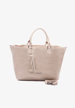 Sac fourre-tout beige avec anses doubles, un pompon décoratif et une bandoulière amovible enroulée à côté sur fond blanc.