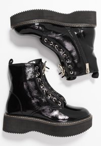 Une paire de bottes noires en cuir verni avec un talon plateforme, des lacets à l'avant, des zips latéraux et des semelles en caoutchouc épaisses, présentée sur un fond blanc.