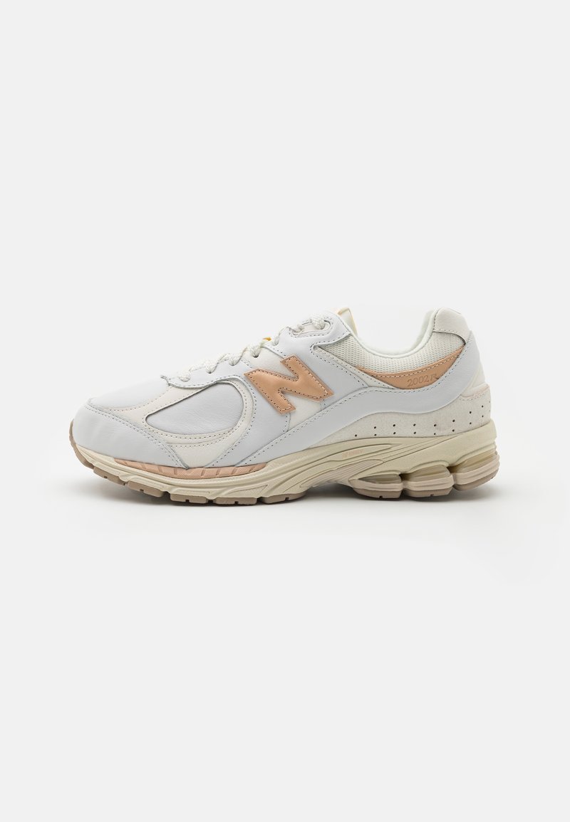 Baskets New Balance 2002R blanches et beiges avec des panneaux en cuir et en mesh, fermeture à lacets, et semelle coussinée sur fond blanc.