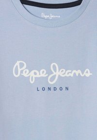 Šviesiai mėlynos spalvos medvilninė marškinėliai su apvalia iškirpte. Priekyje yra užrašas „Pepe Jeans“ baltos spalvos rašysena ir „LONDON“ tamsiai mėlynos spalvos tekstu po juo.