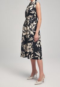 Floral dress in black and cream, sleeveless with a cinched waist. Paired with beige slingback heels featuring a bow detail.