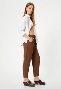 Bruine, lichte stoffen broek met elastische tailleband en zakken. Gecombineerd met een witte overhemd en donkerbruine hakken.