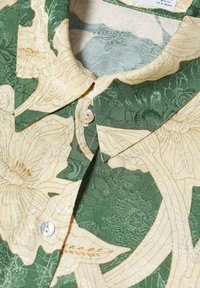Chemise à manches courtes avec un motif floral jacquard vert et beige, dotée d'un col et d'une fermeture à un seul bouton blanc.