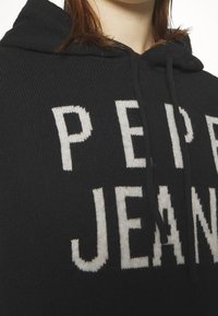 Sweat à capuche en maille noire avec de grandes lettres blanches indiquant « PEPE JEANS ». Tissu texturé avec une coupe décontractée.