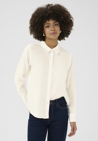White button-up shirt made of lightweight fabric, featuring a classic collar and long sleeves, paired with dark blue jeans.