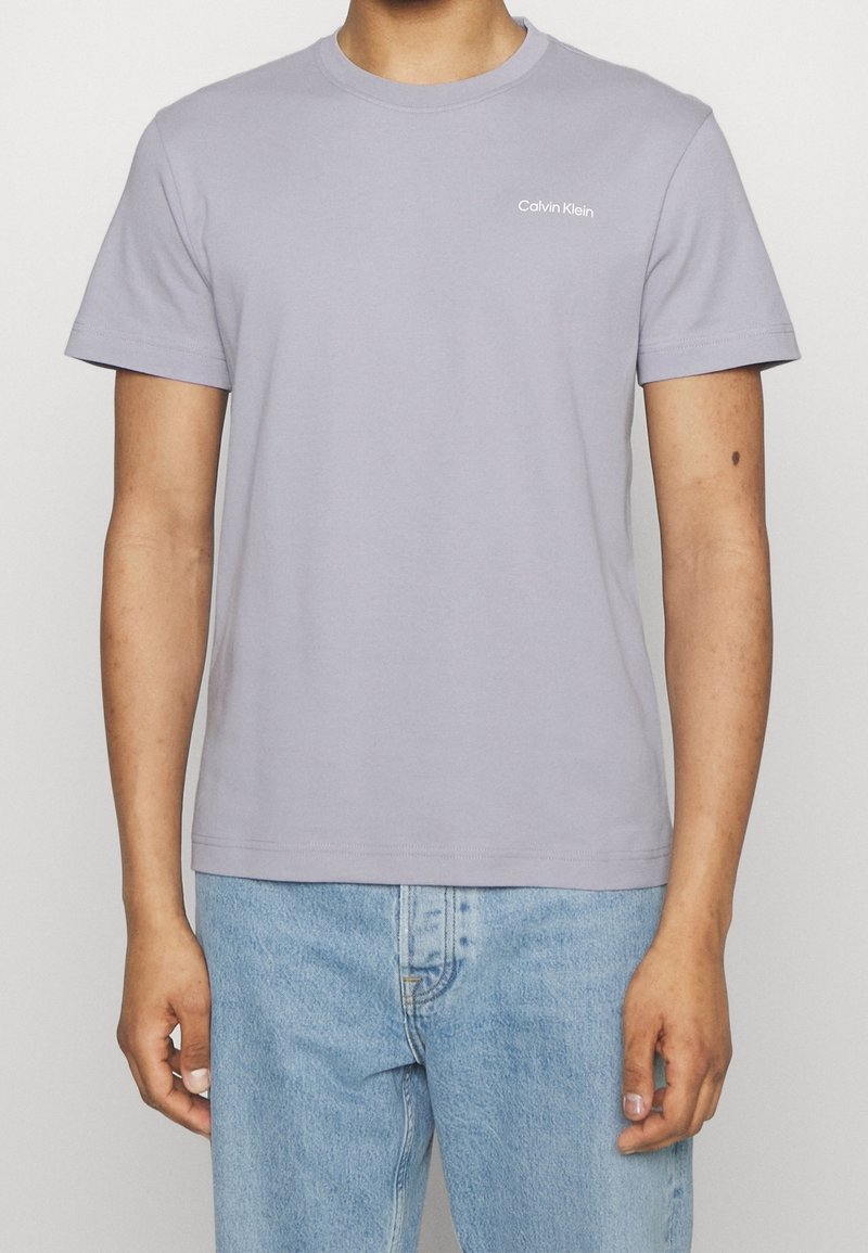 Camiseta de algodón de color púrpura claro con mangas cortas, escote redondo y pequeño logo blanco de "Calvin Klein" en el lado izquierdo del pecho.