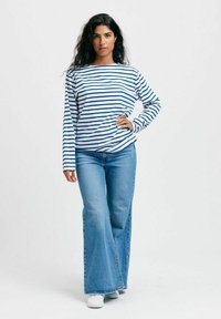 Pitkähihaisen, tummansinisen ja valkoisen raidallisen paidan parina on leveälahkeiset, vaaleansiniset farkut ja valkoiset kengät. Yksinkertaista, rentoa pukeutumista, jossa on väljä kaarroke.