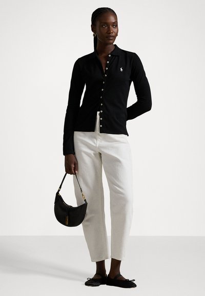 Black long-sleeve polo shirt with button closure and logo; paired with white straight-leg pants and a black handbag. Footwear is flat black shoes.