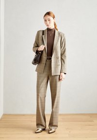Blazer à carreaux et pantalon assorti en beige, avec un col roulé marron, des accents dorés et un sac à main noir. Ajustement sur mesure, longueur jusqu'au sol.