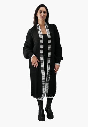 Sort strikket cardigan med hvid stribet kant, lange ærmer og sidelommer. Designet er løstsiddende og knælangt.