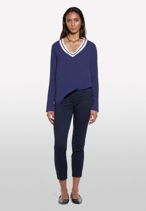 Blusa navy a maniche lunghe con colletto a V bianco, abbinata a pantaloni navy slim-fit e ballerine nere. Tessuto morbido, design casual.