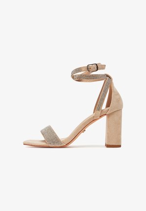 Sandalo beige in pelle scamosciata con tacco a blocco, caratterizzato da una cavigliera ornata di strass e da una fascia larga sulle dita. Tessitura liscia.
