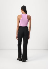 Top a righe rosa e pantaloni neri a campana, con una texture liscia e dettagli a striscia laterale. Scarpe nere completano l'outfit.