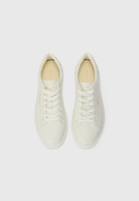 Sneakers bianchi in pelle con punte rotonde, lacci piatti e colli imbottiti. Presentano cuciture laterali testurizzate e un discreto logo dorato.