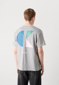 Grå kortærmet t-shirt med et stort geometrisk grafik i blå, grøn og pink på ryggen med "Calvin Klein" tekst under.