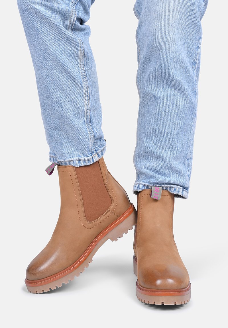 Bruine leren Chelsea boots met elastische zijpanelen, rubberen zolen en paarse trekbands, gedragen met lichtblauwe spijkerbroeken.