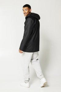 Black waterproof jacket with a hood, long sleeves, and side pockets, paired with gray sweatpants and white sneakers, standing on a light background.