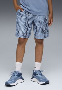 Shorts azuis com padrões de grelha e ondas, feitos de material leve. Combinados com sapatilhas azuis e meias brancas até ao tornozelo.