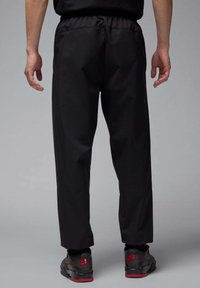 Zwarte sportbroek met elastische tailleband, rechte pijpen en zijnaaddetails, gecombineerd met zwarte sneakers met rode accenten.