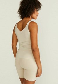 Beige sömlös linne med breda axelband och V-ringning i ryggen, parat med matchande högmidjade shorts, båda tillverkade av mjukt elastiskt material.