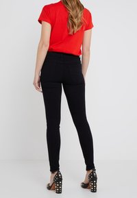 Black skinny jeans with a high waist, featuring back pockets. Paired with a red short-sleeve shirt and black studded heels.
