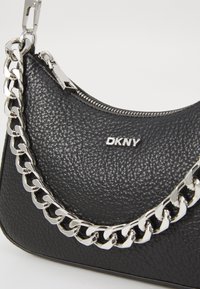 Black leather handbag with a textured finish, featuring a silver chain strap and a zip closure. DKNY logo is prominently displayed.