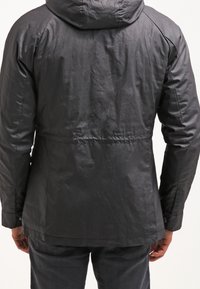 Czarna kurtka z kapturem o teksturowanym materiale zewnętrznym, charakteryzująca się dopasowanym krojem i elastycznym paskiem w talii. Widok z tyłu ukazuje detale szwów oraz mankiety.