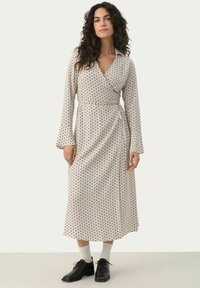 Beige Wickelkleid mit schwarzen Punkten, langen Ärmeln und einem Kragen, mit einem Bindeband in der Taille und einem knieumspielenden Schnitt.