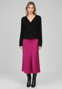 Cardigan noir boutonné en matériau doux et texturé, associé à une robe nuisette en soie magenta et des bottes noires jusqu'aux genoux.