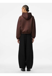 Felpa con cappuccio marrone, dal fit morbido, con orlo a costine e maniche lunghe, abbinata a pantaloni neri larghi. Tessuto liscio e design rilassato.