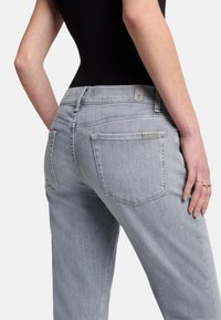 Jeans en denim gris clair avec une coupe décontractée, dotés d'une taille haute, de deux poches arrière et d'une étiquette en cuir minimaliste sur la ceinture.