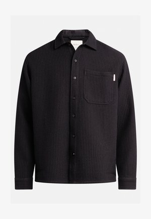 Schwarzes Langarmhemd mit strukturiertem Waffelmuster, Knopfleiste, Kragen und einer einzelnen Brusttasche. Flacher Saum und aufgekrempelte Ärmel.