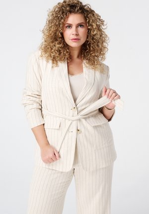 Costume crème clair avec des rayures verticales, doté d'une taille ceinturée, de manches longues et de poches latérales. Tissu doux avec une finition lisse.