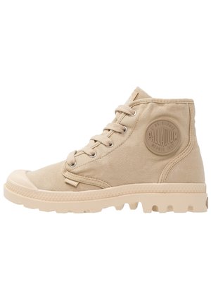 Botte montante beige en toile avec une semelle en caoutchouc texturée, dotée d'un patch logo rond, d'un laçage à l'avant et d'un bout renforcé.