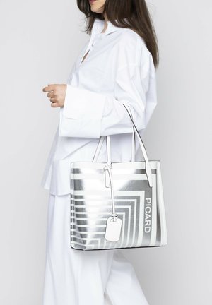 Transparante tas met zilveren en witte geometrische strepen, voorzien van een rechthoekig label, elegante handvatten en een gladde textuur.