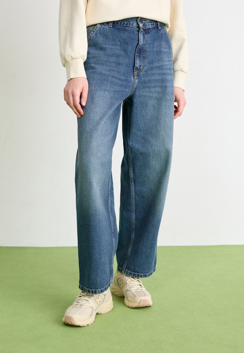 Jean en denim bleu avec une coupe décontractée, taille haute, design traditionnel à cinq poches et décoloration subtile avec une coupe droite.