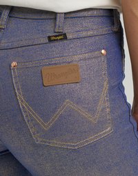 Džínsy v modrej farbe s jemným leskom; majú zlaté stehy a koženú nášivku s názvom značky "Wrangler" na chrbte.