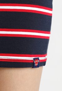 Mörkblå bomulls T-shirt med horisontella röd- och vit-randiga linjer. Synlig etikett "SUPER DRY" vid fållen, med blå bakgrund och vit text.