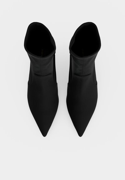 Paire de bottines noires à bout pointu vues de dessus sur fond blanc, bottes debout et parallèles.
