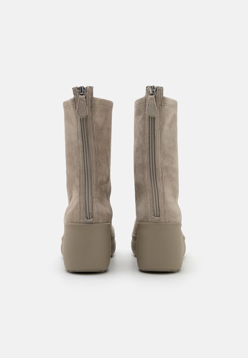 Beige Wildleder-Stiefeletten mit zwei seitlichen Reißverschlüssen, runder Zehenpartie und dicker Gummisohle. Glatte Textur mit matter Oberfläche.