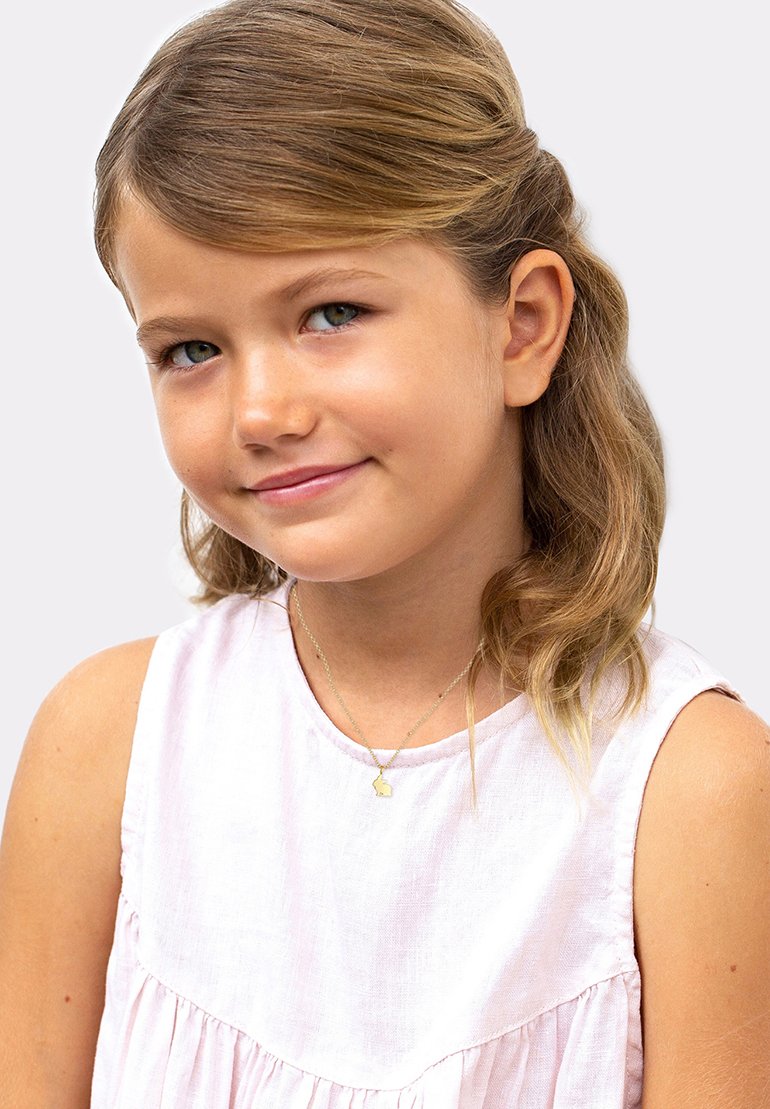 Lys rosa linnedress med en rynket kant. Barnet bærer en guld halskæde med en lille, genkendelig charme. Glat, lige hår.