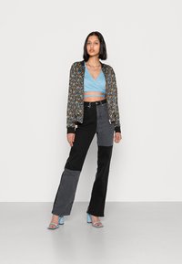 Jacket bomber floral com detalhes em preto, top cropped azul claro e calças de cintura alta em patchwork nas cores preto e cinza. Sandálias de salto azul claro.