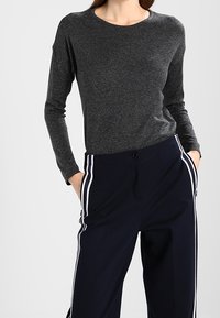 Graues Langarmshirt mit rundem Halsausschnitt, kombiniert mit dunkelblauen Hosen mit weißen Seitenstreifen und einer lässigen Passform.