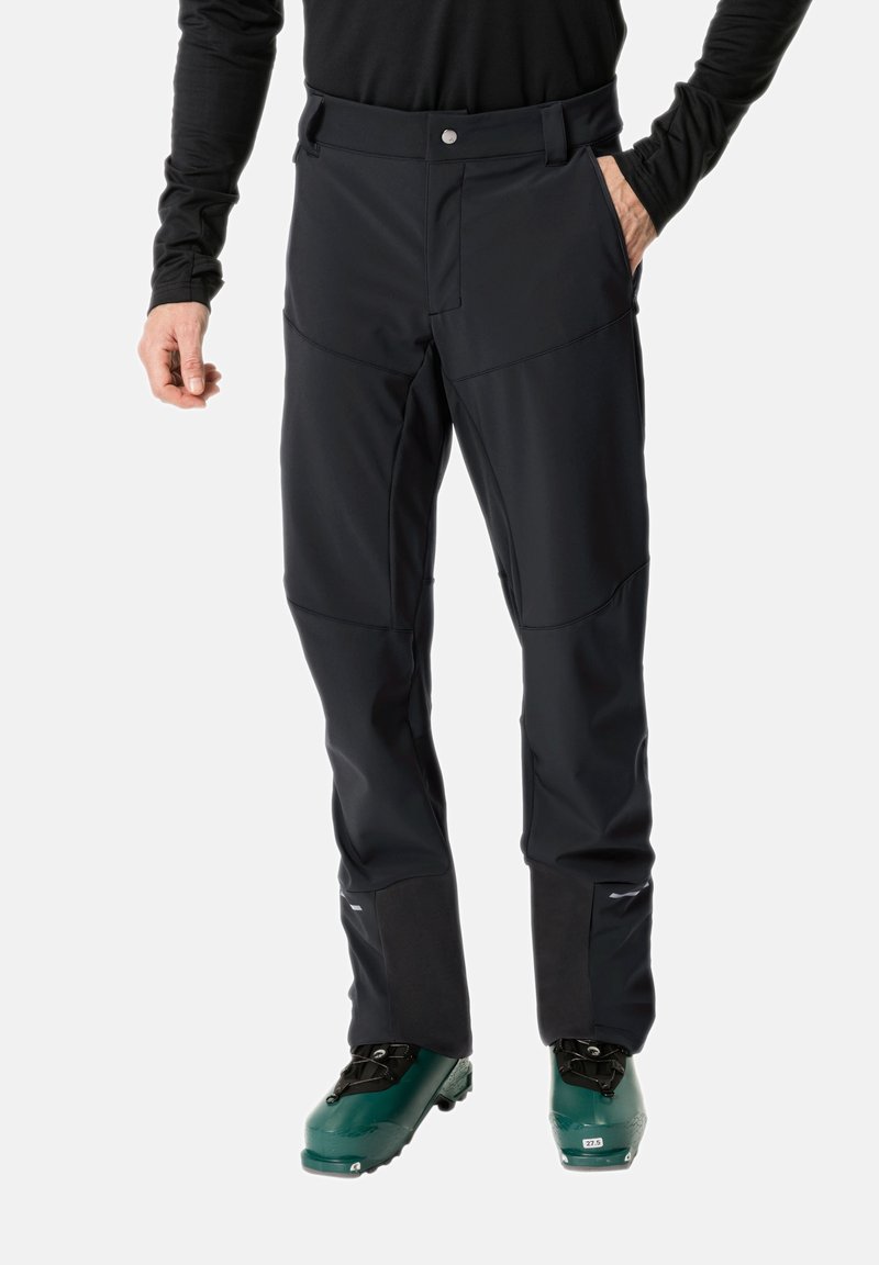 Pantalones de esquí negros con bolsillos y piernas inferiores reforzadas, con una textura suave y un diseño ajustado, combinados con botas de esquí verdes.