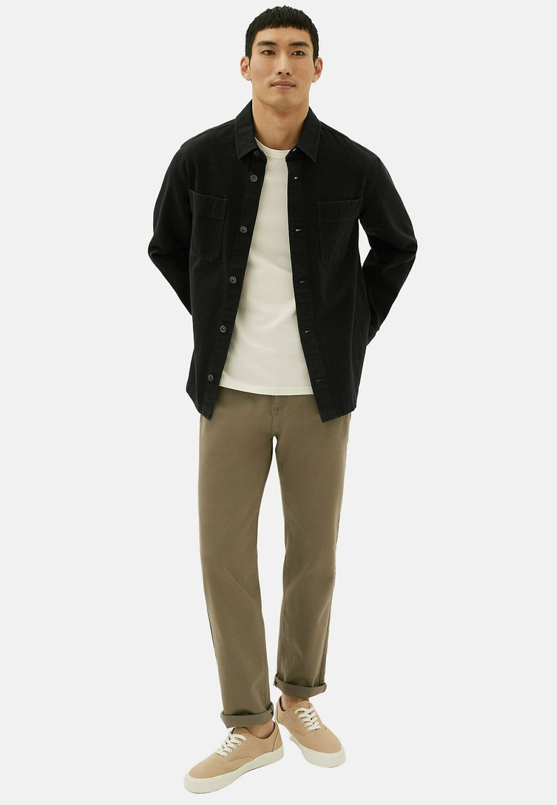 Chemise noire à boutons sur t-shirt blanc, associée à un pantalon kaki et des baskets beiges. Comprend deux poches poitrine et une coupe regular.