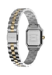 Timex-klocka med ett silverfärgat band i rostfritt stål med gulddetaljer, rektangulärt urtavla och en framträdande krona. Baksidan är märkt med modellinformation.